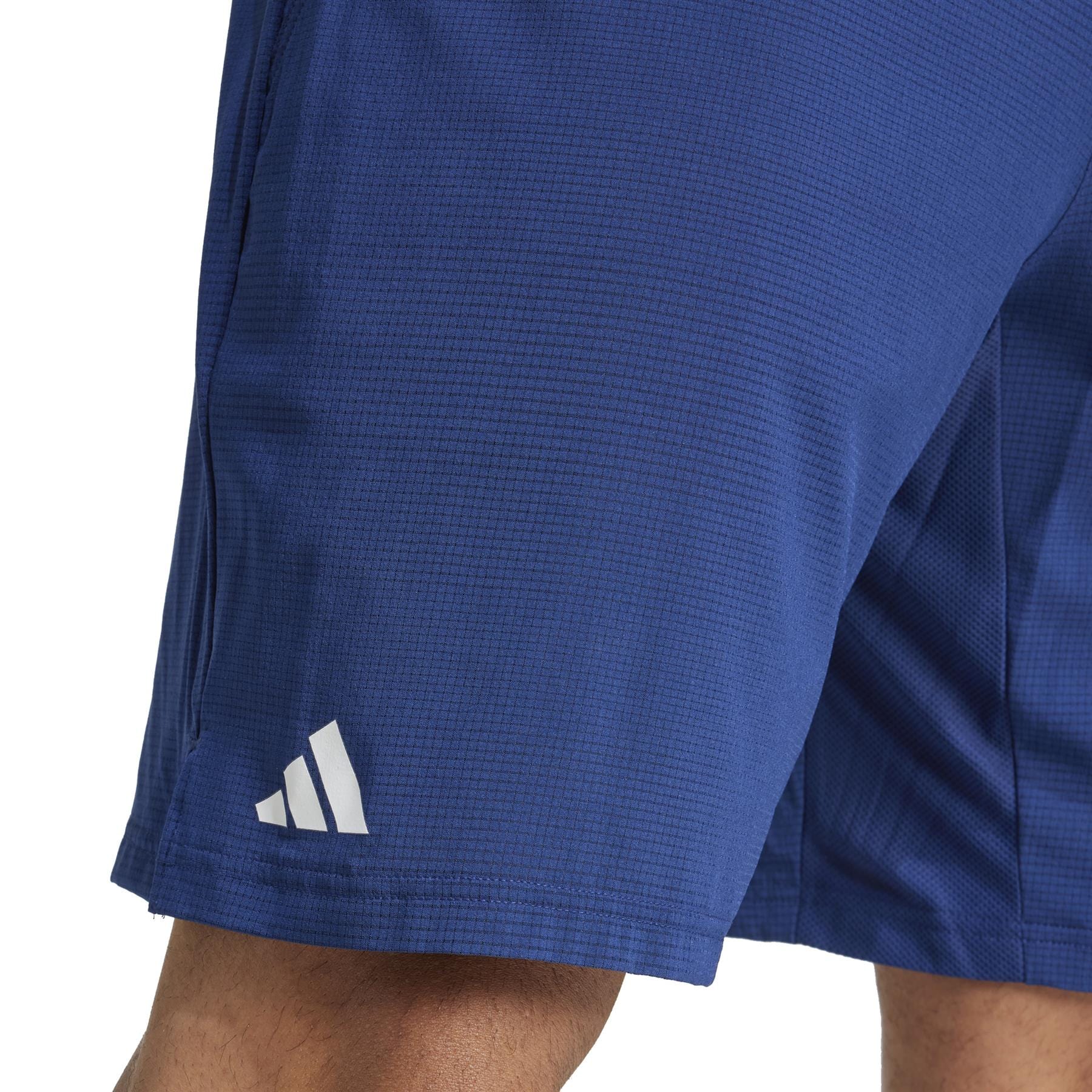 Close-up of a person wearing adidas ADIDAS Ergo Men's Badminton Shorts in navy, showcasing the white Adidas logo on the left. Made from recycled materials with a subtle grid pattern, these lightweight shorts are ideal for badminton enthusiasts who value style and sustainability.