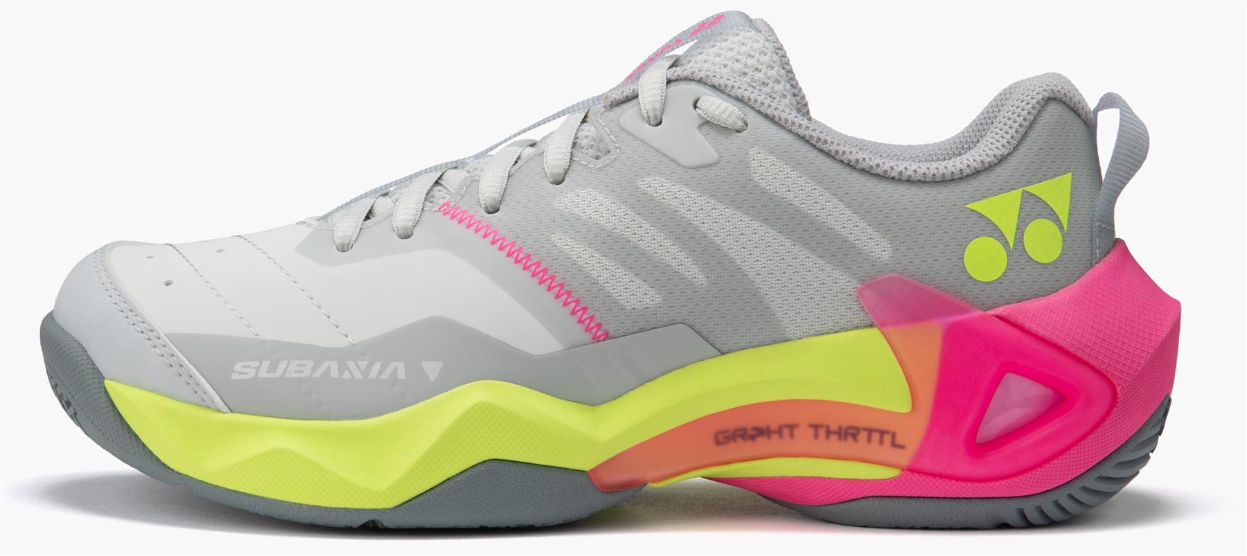 The Yonex Subaxia GT Women's Badminton Shoes in light grey, featuring neon yellow and pink accents, a thick sole with GRPHT THRTTL technology, the Yonex logo on the heel, and "Subaxia V" on the side.