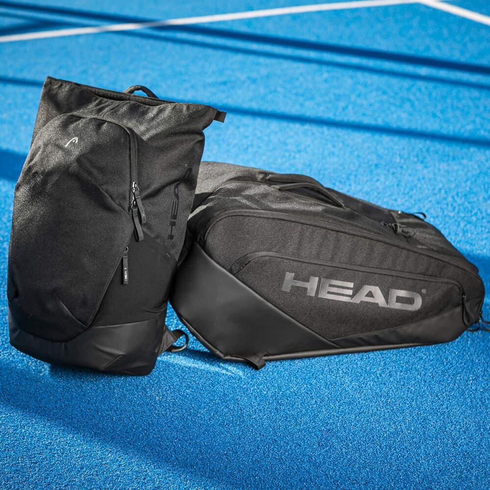 Two black HEAD Pro X Badminton Backpack 25L bags rest on a blue tennis court. Their modern urban style and prominent HEAD logo stand out sharply against the white lines in the background.