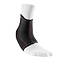 A close-up of an ankle wearing a white sock with the McDavid Ankle Sleeve, a black neoprene brace featuring red stitching and a textured surface for optimal support and compression therapy. This sleeve extends from the ankle to just above the foot, ensuring comfort and stability.