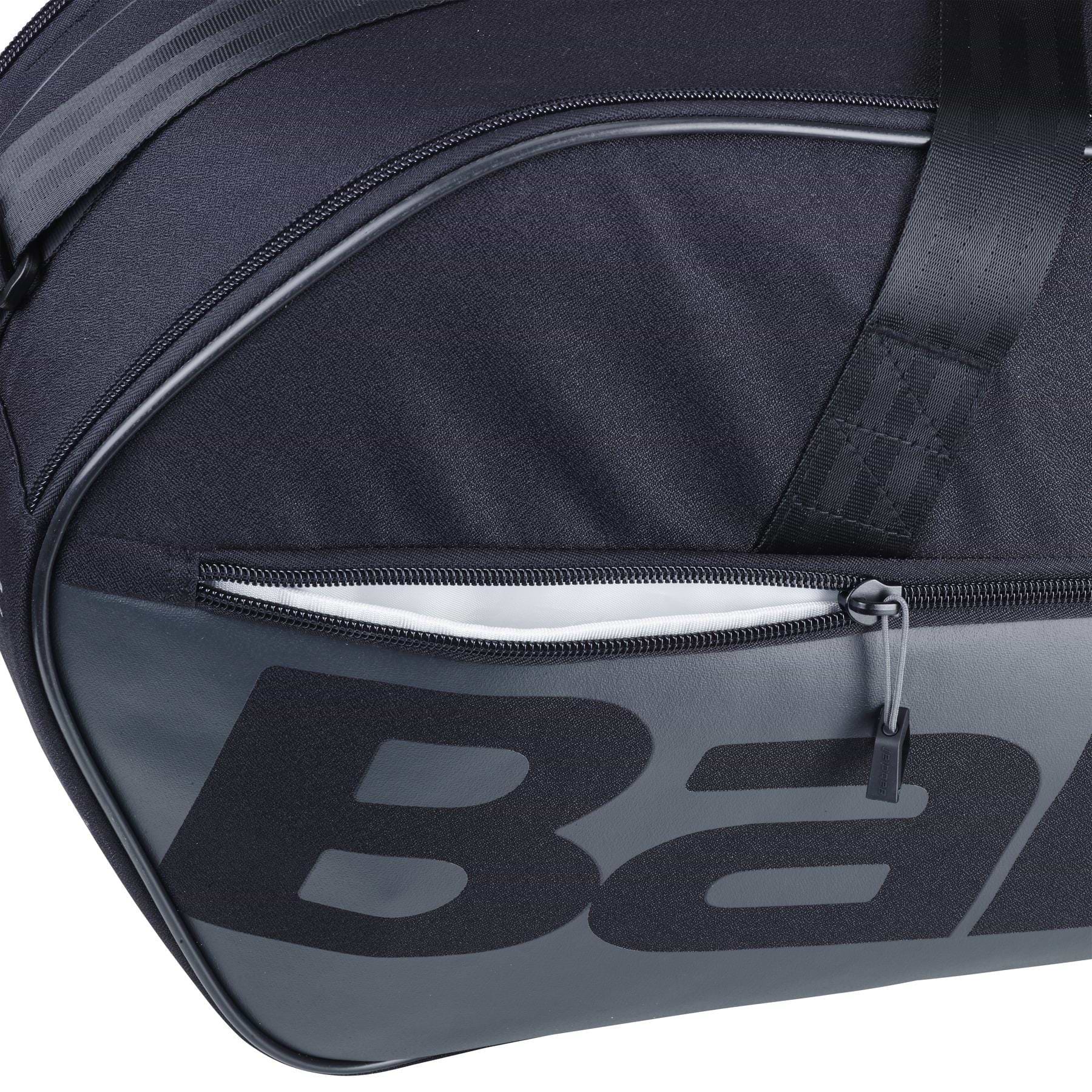 Close-up of the Babolat Court M 6 Racket Badminton Bag in black, showcasing a zippered pocket and bold lettering. Made from recycled PET, the durable fabric and prominent zip pull emphasize its sleek design.