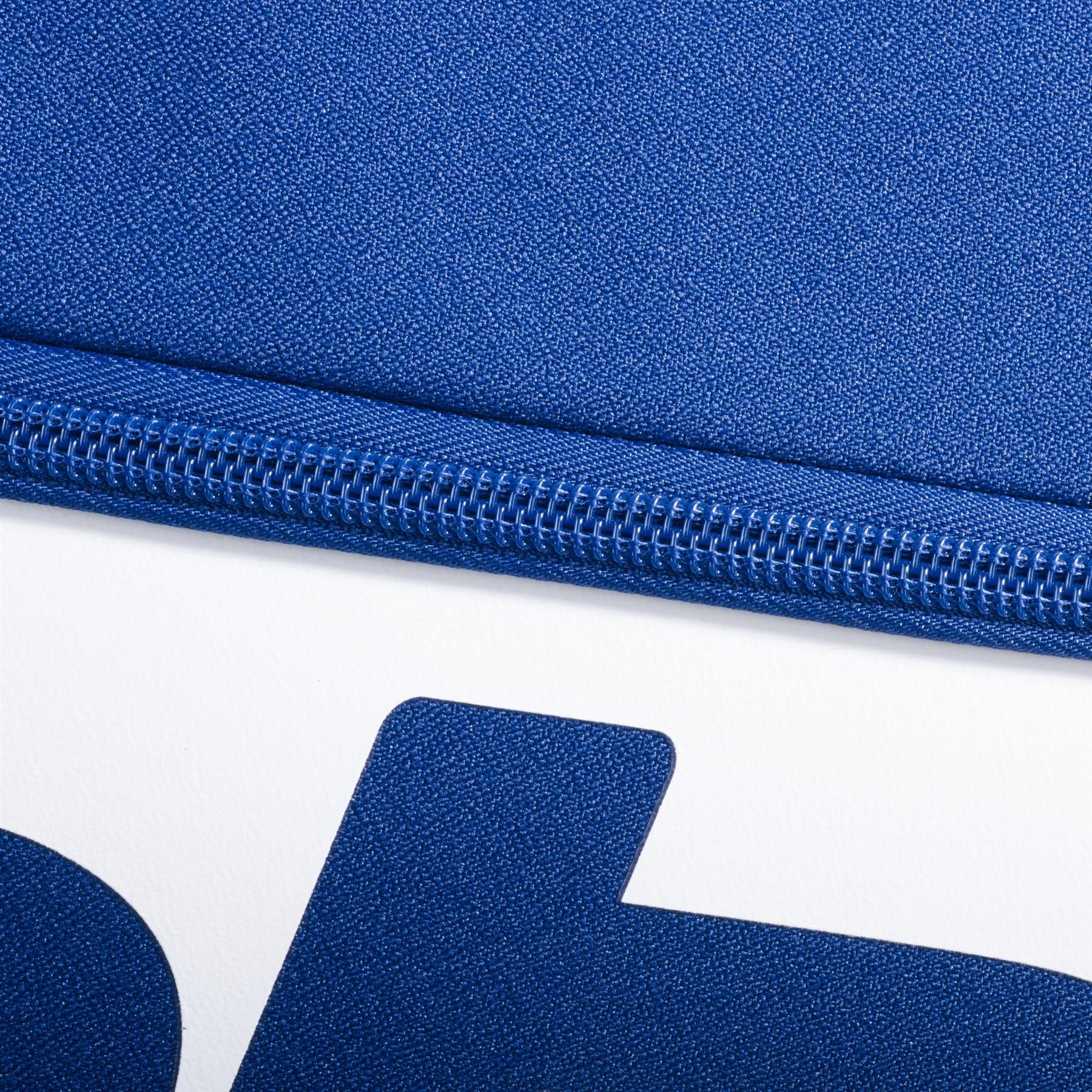 Close-up of a blue zipper on textured dark blue fabric from the Babolat Court M 6 Racket Badminton Bag, made with recycled PET, shown above a white surface with a bold partial blue letter. Brand: Babolat.