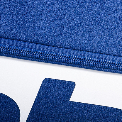 Close-up of a blue zipper on textured dark blue fabric from the Babolat Court M 6 Racket Badminton Bag, made with recycled PET, shown above a white surface with a bold partial blue letter. Brand: Babolat.