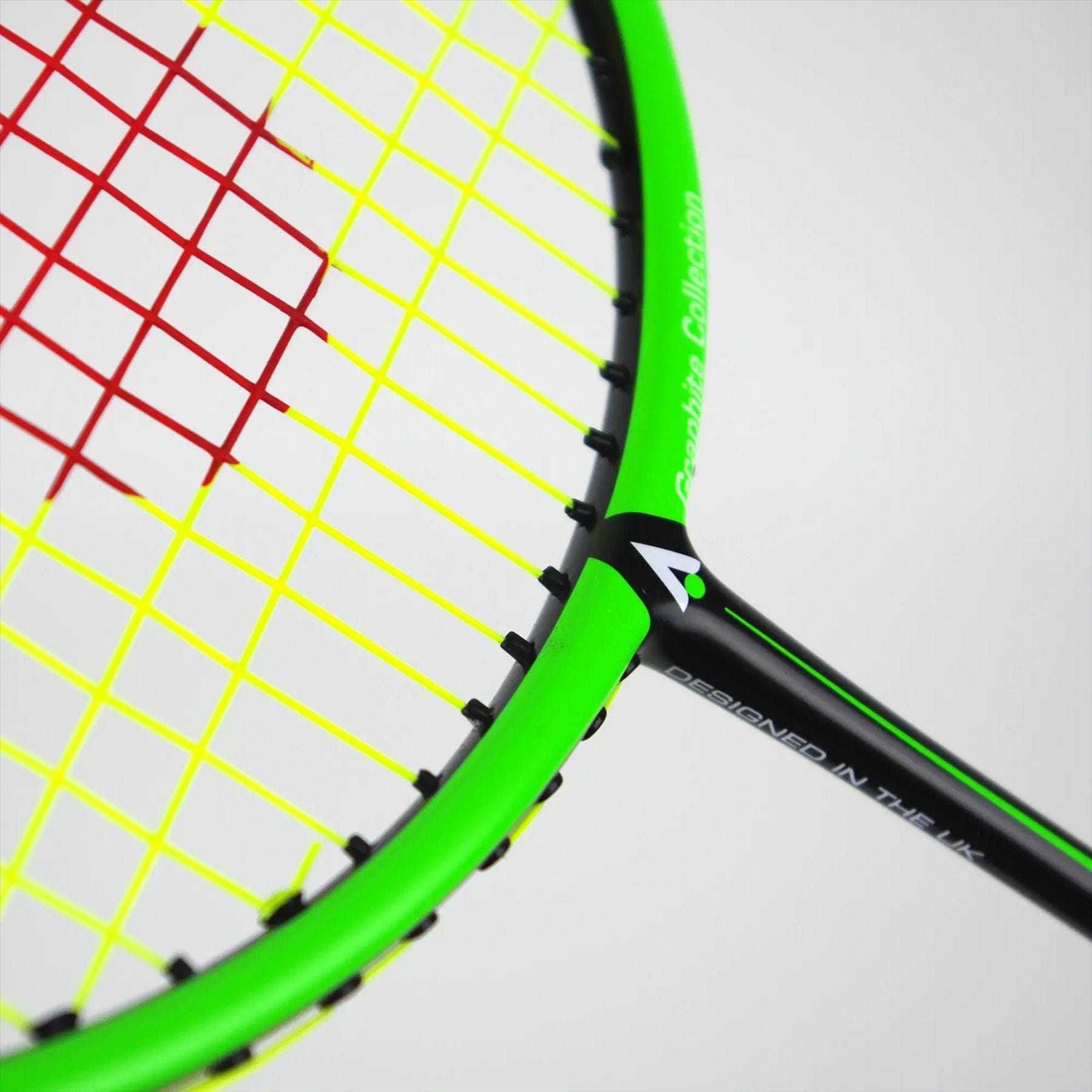 A close-up of the vibrant Karakal Black Zone BZ 20 2.1 badminton racket shows its black and green frame with red and yellow strings. The isometric head enhances playability, and the frame proudly displays a white logo stating "DESIGNED IN THE UK.