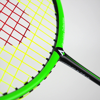 A close-up of the vibrant Karakal Black Zone BZ 20 2.1 badminton racket shows its black and green frame with red and yellow strings. The isometric head enhances playability, and the frame proudly displays a white logo stating "DESIGNED IN THE UK.
