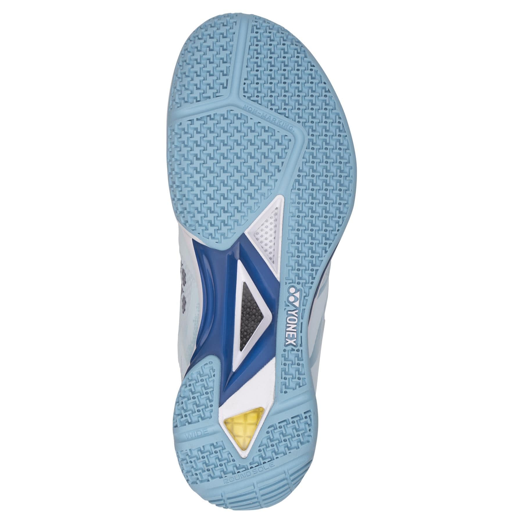 The image displays the sole of Yonex Power Cushion Eclipsion Z3 Wide Men's Badminton Shoes in light blue, showcasing a patterned grip with a yellow triangular section. The center features a visible Yonex logo, complemented by white and blue accents highlighting its Power Cushion for enhanced stability.