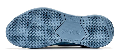The image shows the teal blue sole of Yonex Power Cushion Strider Ray Unisex Badminton Shoes, featuring a textured, non-marking grip pattern for shock absorption with "ERGOSHAPE" and "NON-MARKING" branding.
