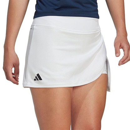 A person wearing the ADIDAS Women's Club Badminton Skirt in white and a dark blue top is standing with their arms relaxed. The skirt, designed by adidas, showcases AEROREADY technology and has a small black logo on one side. The background is not visible.