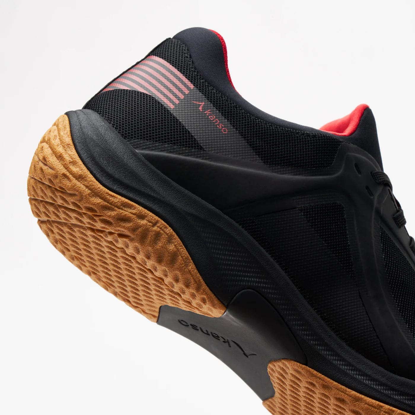 Close-up of the black Kanso Equilibrium EQx3 Unisex Badminton Shoe, featuring orange-brown soles with Speedlight foam for comfort, red heel accents, and a textured tread. The shoe is angled with the sole visible against a white background.