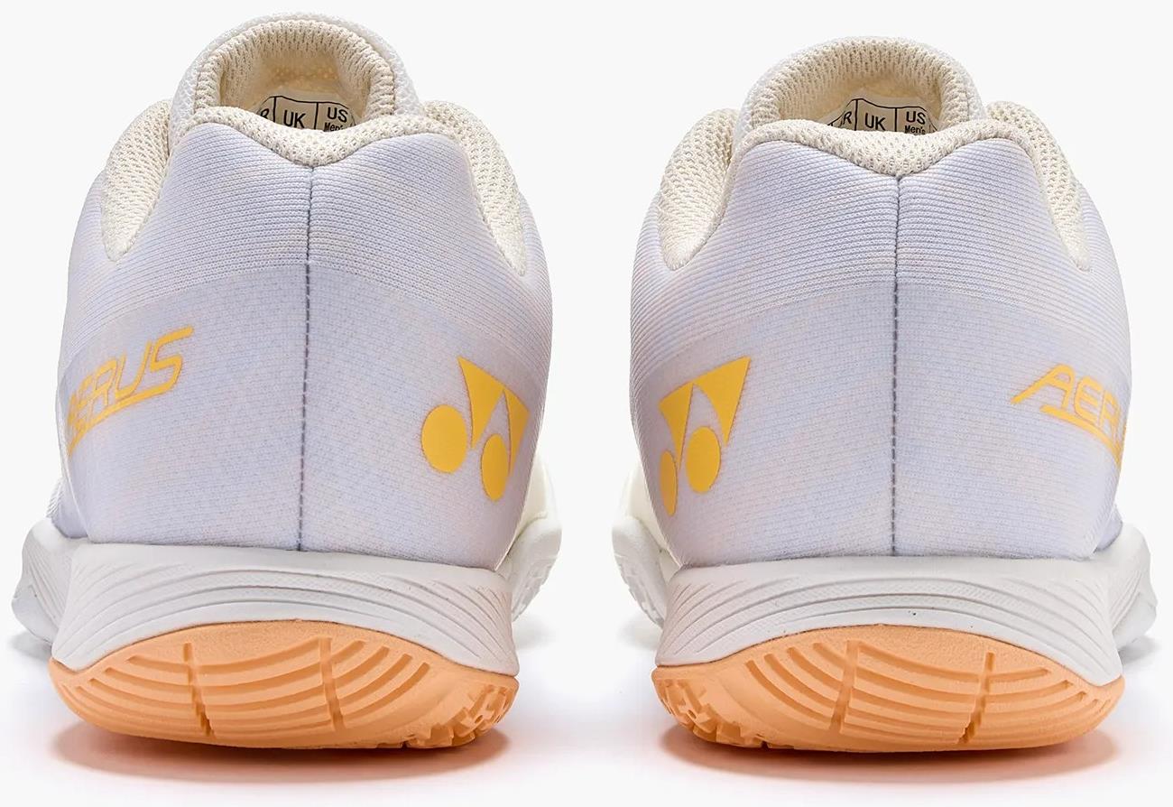 The Yonex Power Cushion Aerus Z2 Women's Badminton Shoes in white and orange feature light orange Yonex logos and accents on the heels, plus matching orange soles, shown here from the back.