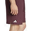 Someone is wearing ADIDAS Ergo Men's Badminton Shorts in Ruby, displaying part of their hand and leg. These maroon shorts have a white adidas logo, a small side slit for mobility, and feature HEAT.RDY technology to keep you cool during intense matches.