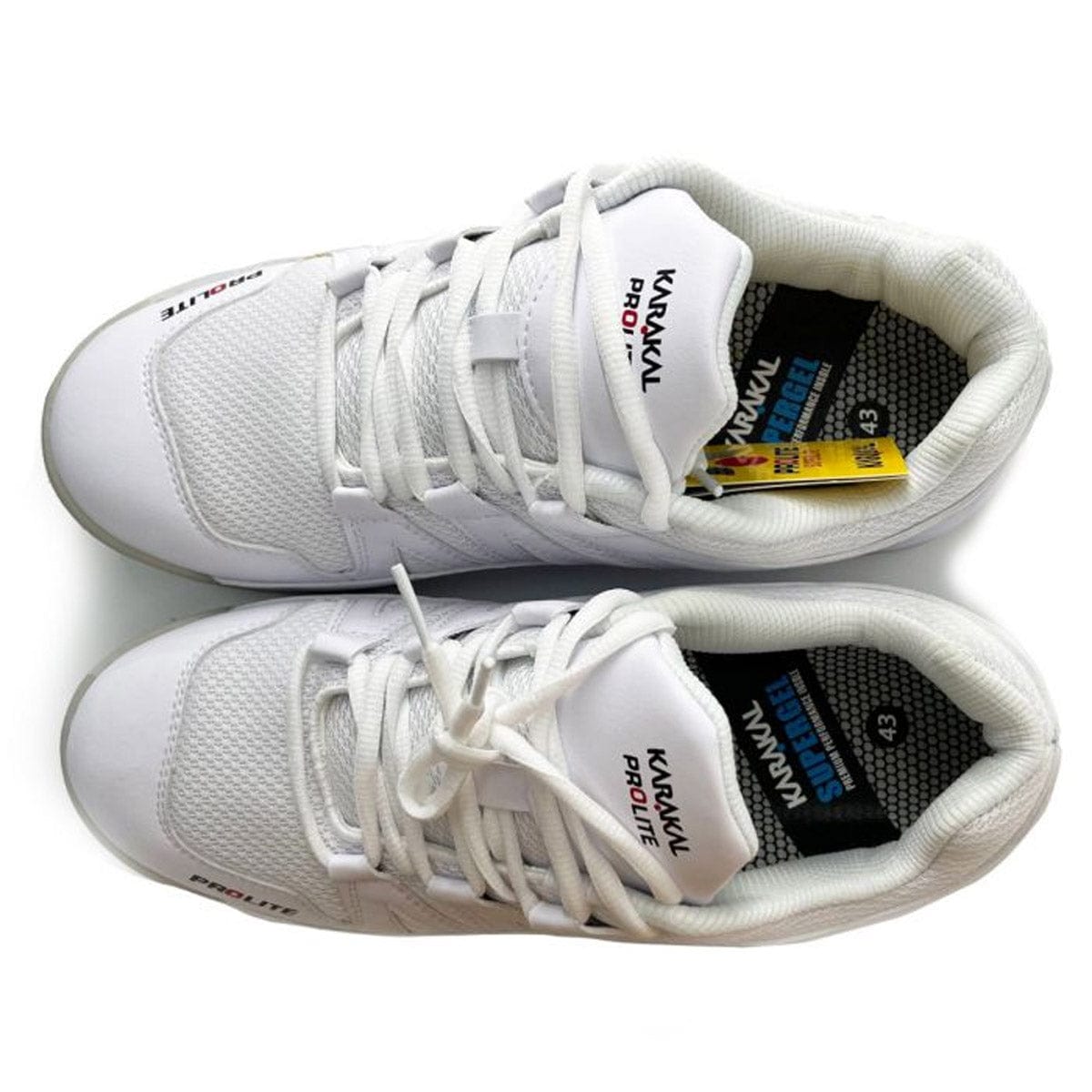 A pair of the Karakal KF Pro Lite Badminton Shoes in white, featuring black and red accents, provides lateral stability. These shoes have a tag on one shoe and text on the tongue and outer side. Displayed from above, you can see their shock-absorbing gel insoles with a black-and-white pattern.