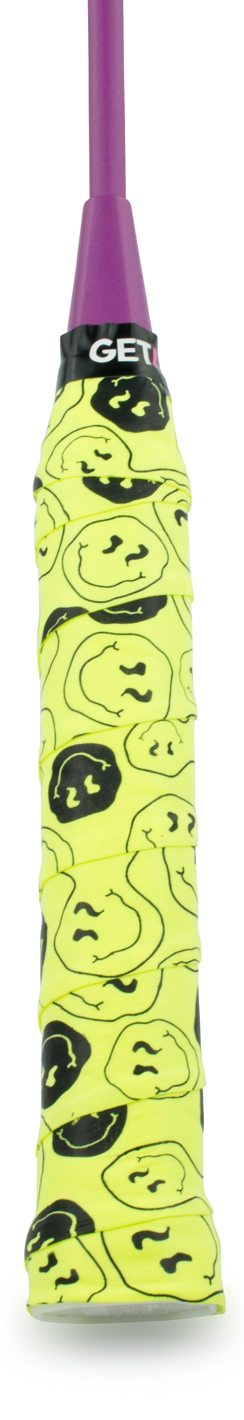 A close-up of the Get a Grip Badminton Overgrip - Smiley by Get A Grip, featuring a yellow grip with black smiley face doodles and a purple handle—an ideal badminton gift.