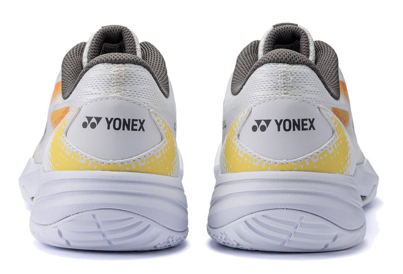 A pair of Yonex Power Cushion Cascade Accel Unisex Badminton Shoes in white and orange, displayed from the back on a white background. This intermediate model from Yonex delivers both style and performance, providing comfort and support for players on the court.