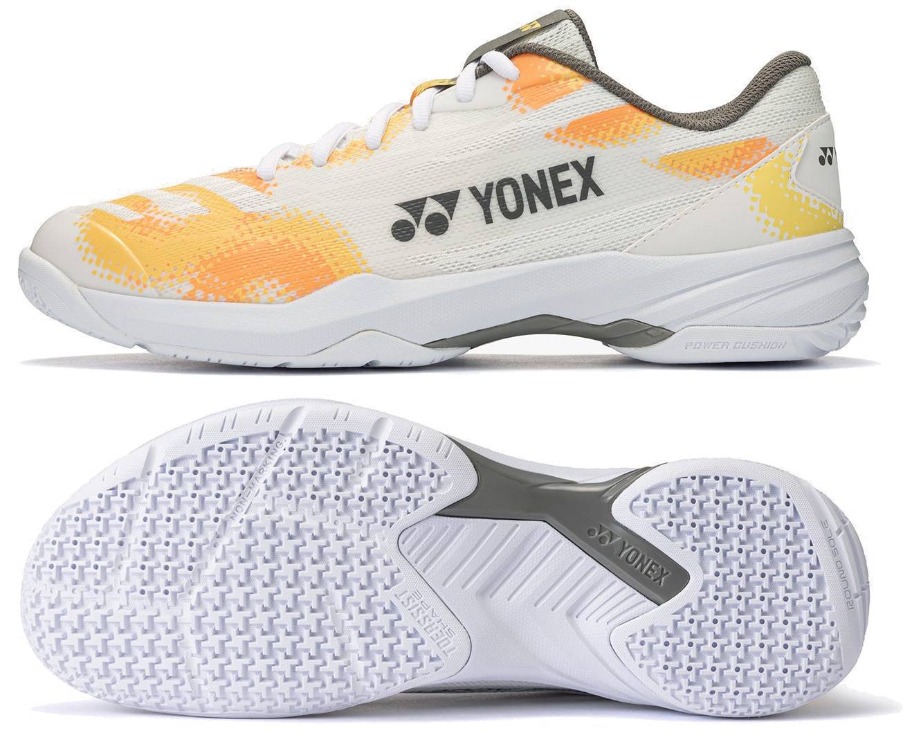 The Yonex Power Cushion Cascade Accel Unisex Badminton Shoes in white and orange with gray accents are displayed from both the side and bottom perspectives. The side view features the distinctive Yonex logo, while the sole showcases textured patterns designed for enhanced grip. This intermediate-level model combines style and performance, making it an excellent choice for enthusiastic players.