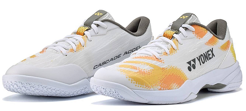 A pair of Yonex Power Cushion Cascade Accel Unisex Badminton Shoes in white and orange, featuring gray laces, textured white soles with renowned Yonex Power Cushion technology, and positioned side by side as an ideal choice for intermediate players.