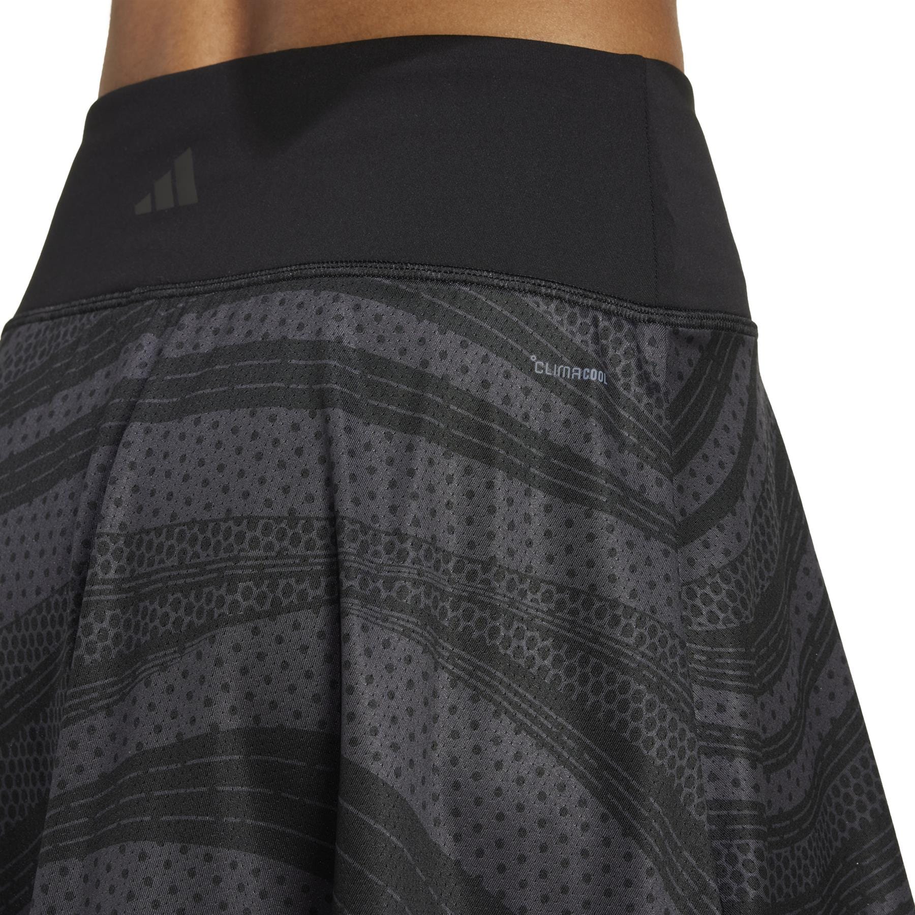 A close-up shows someone wearing the ADIDAS Women's Club Graphic Black Badminton Skirt, featuring a textured pattern, iconic logo, and "Climacool" on the waistband in a flowy design.
