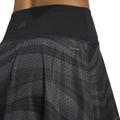 A close-up shows someone wearing the ADIDAS Women's Club Graphic Black Badminton Skirt, featuring a textured pattern, iconic logo, and "Climacool" on the waistband in a flowy design.
