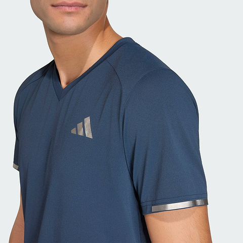 A person wears the ADIDAS Climacool+ Freelift Pro Mens Badminton T-Shirt - Aurora Ink by adidas, a blue V-neck with metallic silver accents and advanced cooling, against a plain light background.