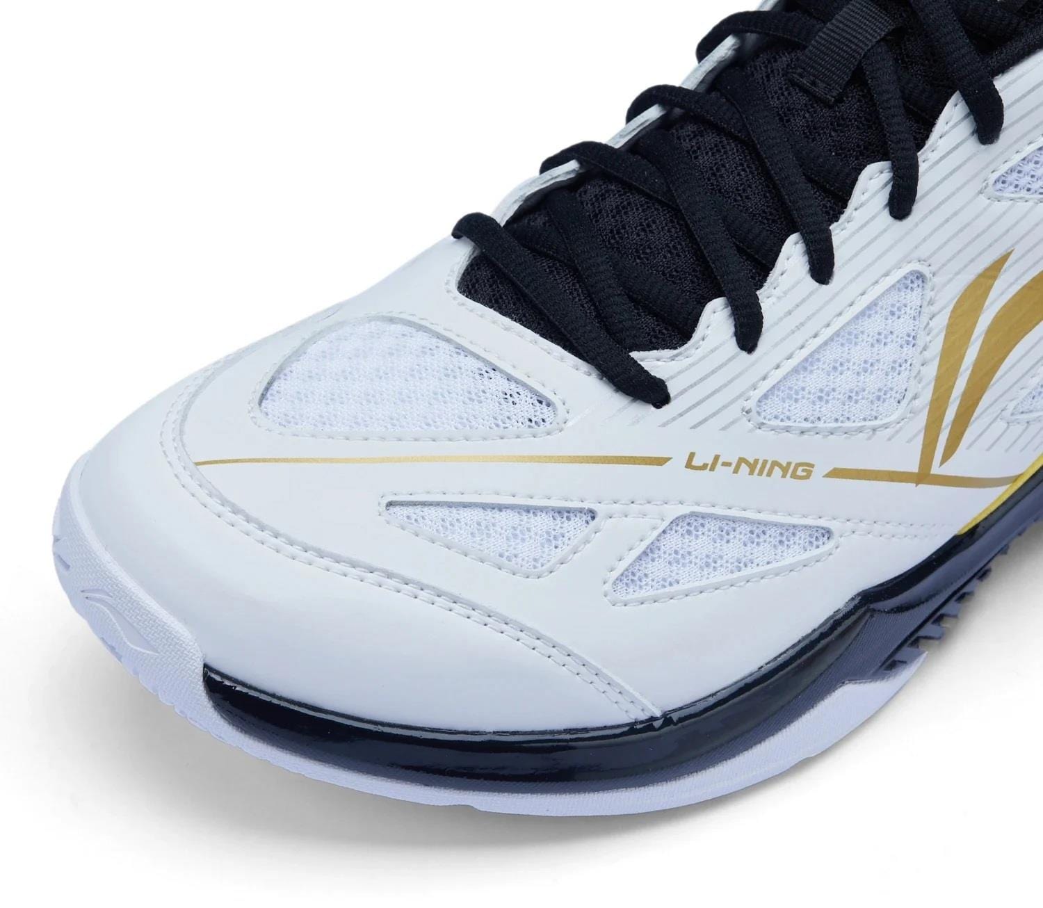 Close-up of Li-Ning Blast JF-01 Lite Unisex Badminton Shoes in white, black, and gold, featuring mesh texture, high-traction outsole, black laces, and the Li-Ning logo on the side.