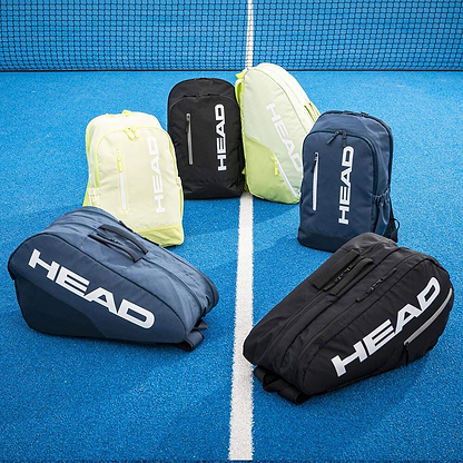 Six HEAD BASE Badminton Backpack 17L - Navy bags are displayed on a blue court near the net, with three standing at the back and three lying in front; each backpack offers a spacious compartment for your badminton gear.