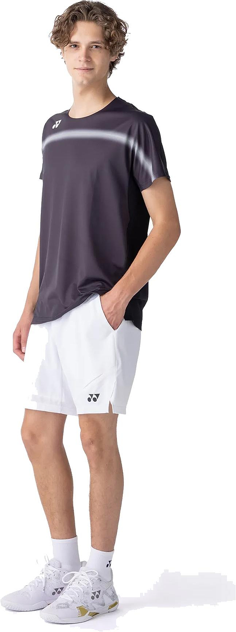 A young person with curly hair poses against a plain white background, wearing the Yonex 10711YX Crew Neck Men's Badminton T-Shirt in black, paired with white shorts, socks, and athletic shoes.