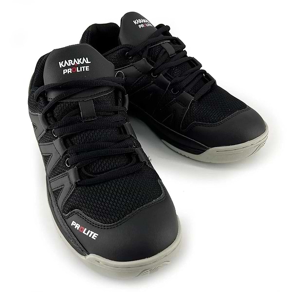 A pair of Karakal KF Pro Lite Badminton Shoes in the new black color is displayed, showcasing white branding, black laces, and gray soles. These shoes feature a mesh design on the upper for enhanced breathability and include a shock-absorbing gel insole for superior comfort. Additionally, they offer excellent lateral stability to support dynamic movements.