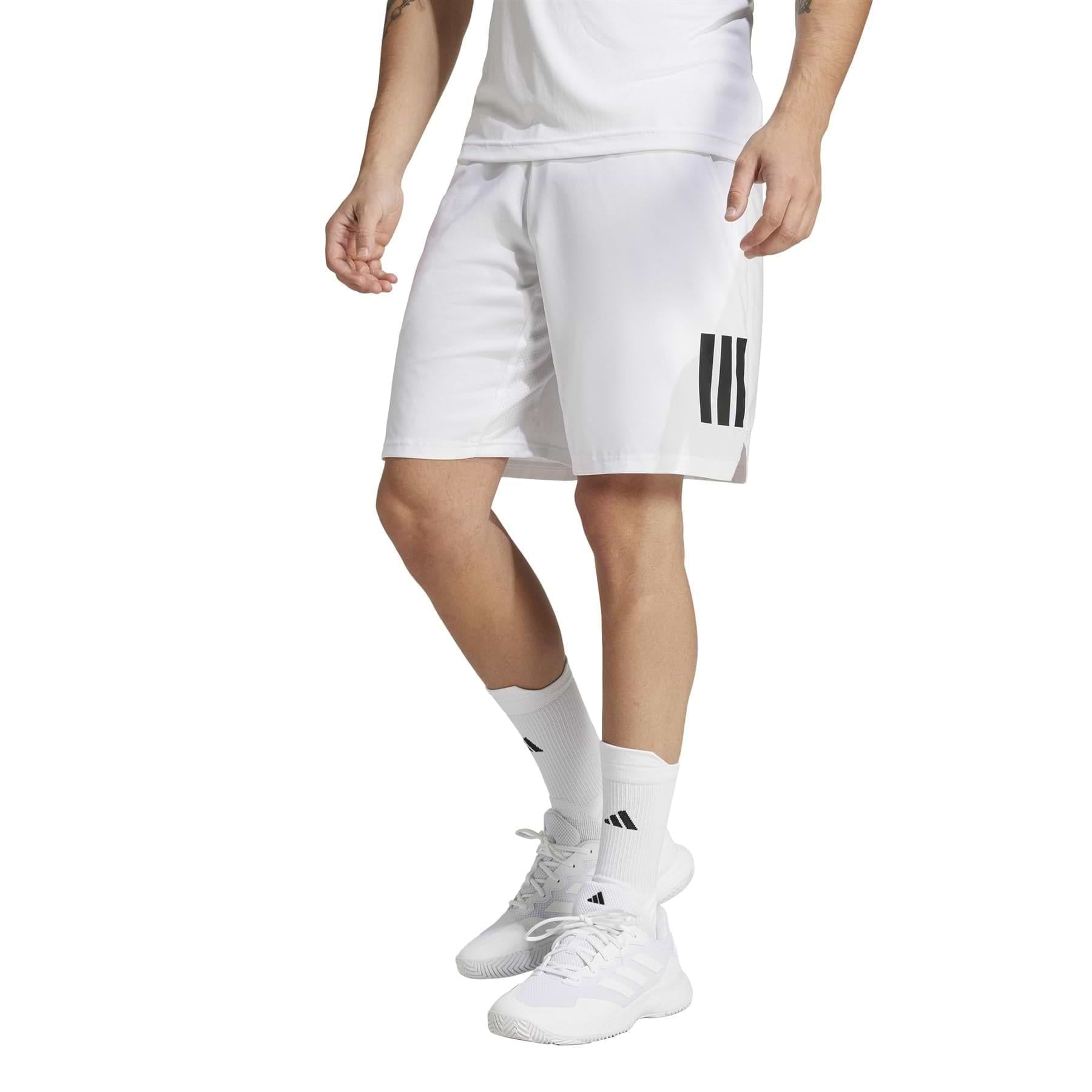 A person wearing a white t-shirt, adidas Men's 3 Stripe Badminton Shorts in white, moisture-wicking white socks, and white sneakers stands against a plain background.
