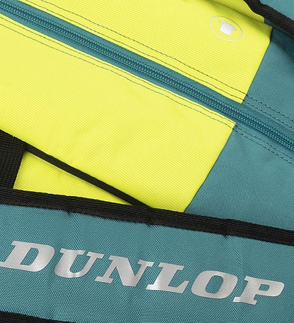 The Dunlop SX Performance 12 Racket Badminton Bag features a dual-color design in teal, black, and yellow. It prominently showcases the "Dunlop" logo on a teal strip, holds up to 12 rackets, includes padded shoulder straps for comfort, and has a circular cup-like icon near the zipper.