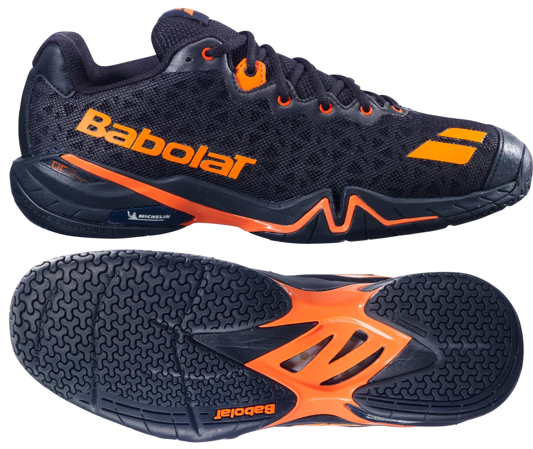 The Babolat Shadow 4 Men's Badminton Shoes in black and orange are shown from the side and sole views, featuring a mesh upper with "Babolat" branding and a textured rubber sole highlighted with orange accents.