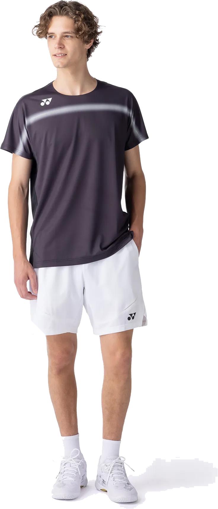A young man wearing a Yonex 10711YX Crew Neck Mens Badminton T-Shirt in black stands facing slightly left with one hand in his pocket, looking off to the side.
