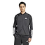 A person is wearing an ADIDAS Men's 3 Stripe Knit Badminton Jacket in black with white sleeve stripes. They stand against a plain white background with hands in their pockets.