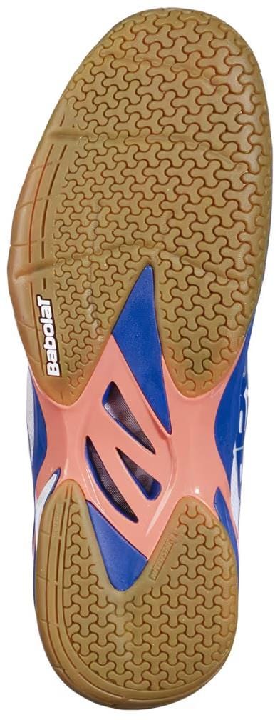 The image shows the sole of the Babolat Shadow 4 Men's Badminton Shoes in White/Blue/Navy, featuring a tan rubber tread with zigzag grip pattern, blue and orange accents, and the Babolat logo near the heel.