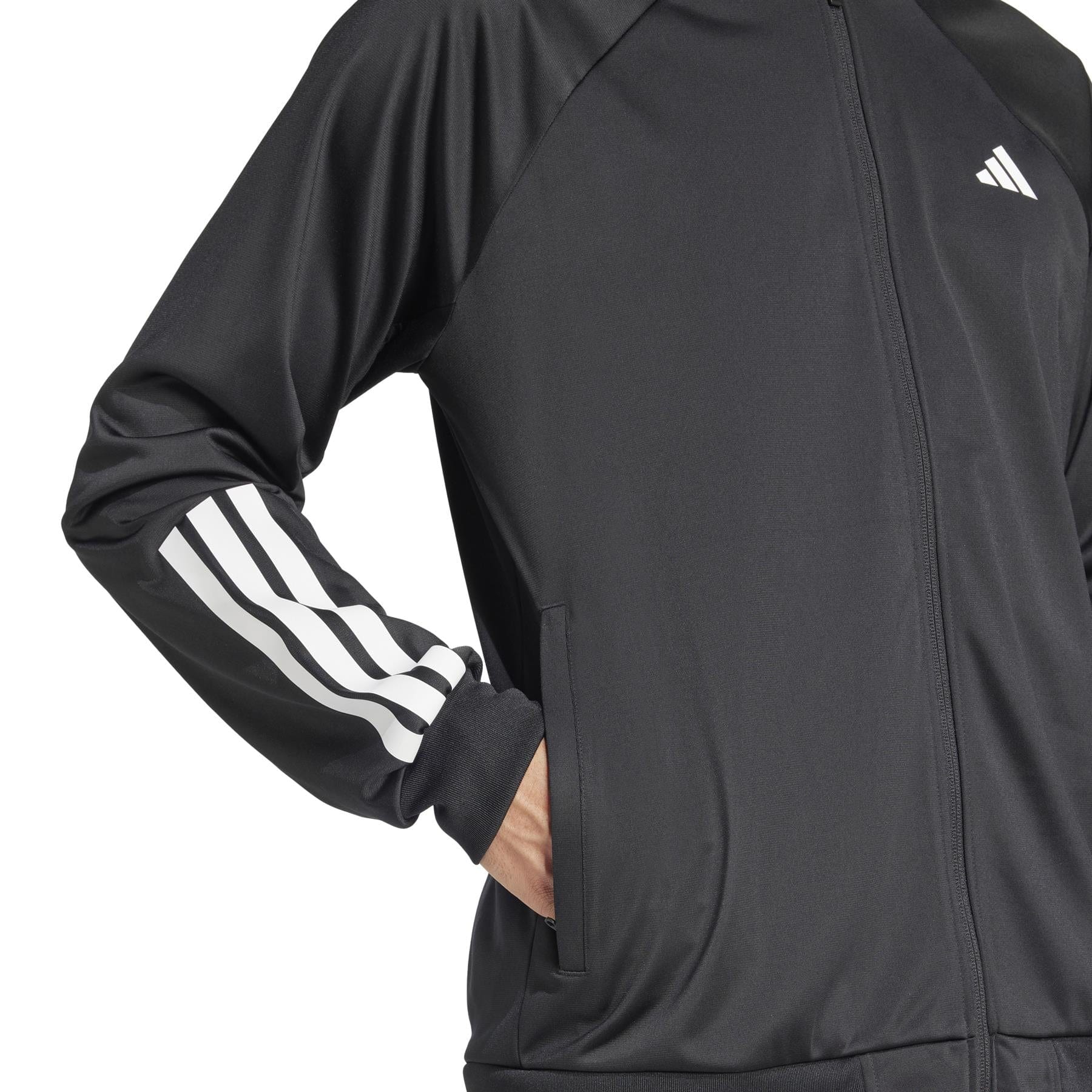 A person is wearing an ADIDAS Men's 3 Stripe Knit Badminton Jacket in black, featuring white stripes on the sleeves and a small upper chest logo, with hands tucked into pockets against a plain white background.