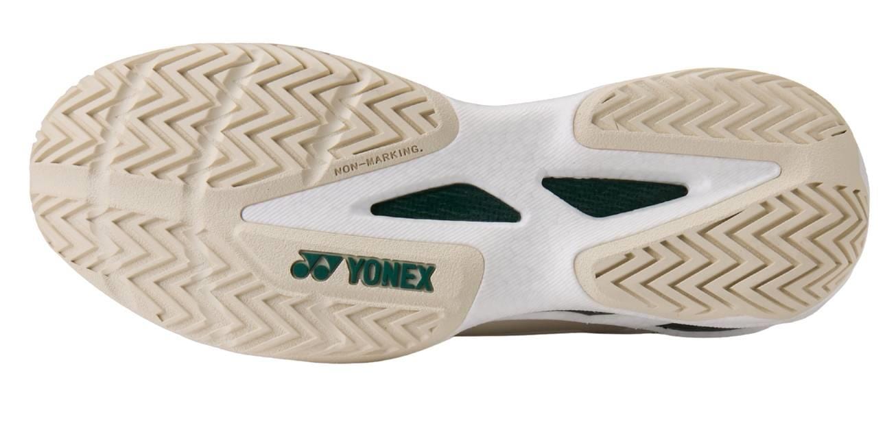 The image shows the beige sole of the Yonex Power Cushion GRPHT THRTTL Concept men's badminton shoe, featuring herringbone tread, a non-marking label, and a green Yonex logo on the white midsection.