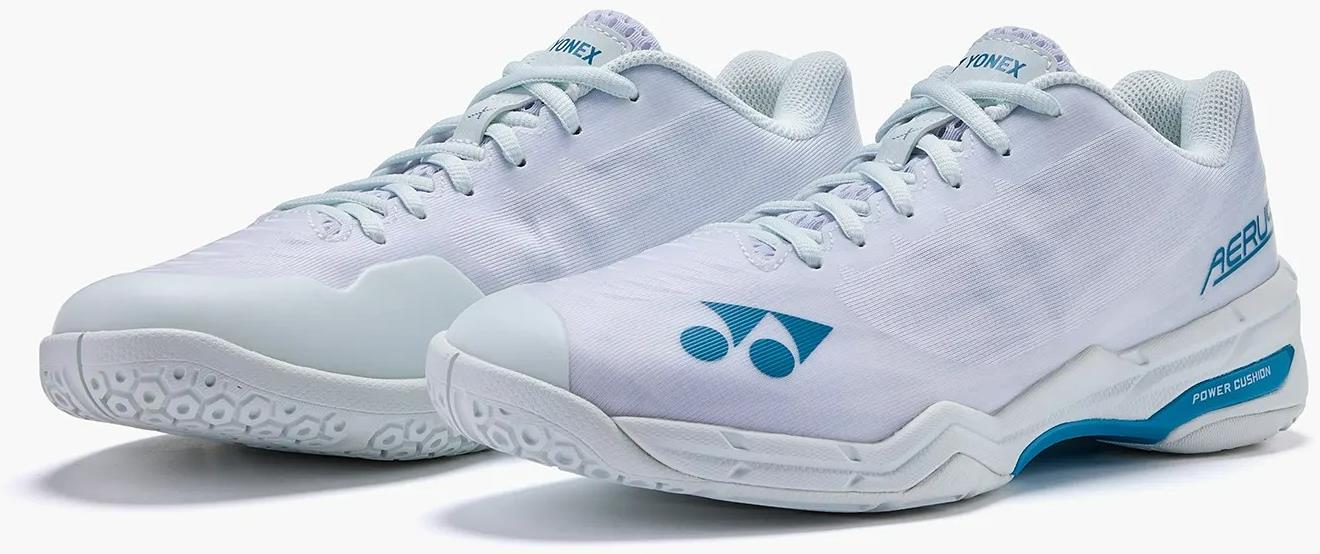 The Yonex Power Cushion Aerus X2 Unisex Badminton Shoes in white with blue accents feature a textured sole and Yonex logo on the side and tongue. Lightweight indoor court shoes, designed for athletic use, shown side by side.