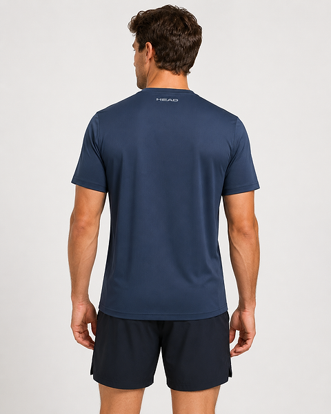 A man, facing away from the camera in black shorts, wears a navy HEAD Club Tech 25 Men’s Badminton T-Shirt by HEAD. This breathable shirt with moisture transfer microfiber has "HEAD" printed on the upper back against a light background.