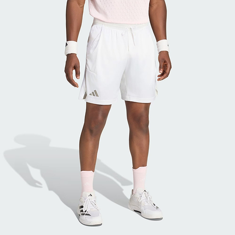 A person wearing adidas ADIDAS Climacool Ergo Pro Men’s Badminton Shorts in white, along with white and pink sneakers, pink socks, a pink shirt, and white wristbands, is standing against a light background. Only the lower half of their body is visible.