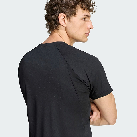 A man with curly hair, wearing the black adidas Climacool+ Freelift Pro Mens Badminton T-Shirt—renowned for its advanced cooling technology—stands with his arms crossed, gazing to his right against a plain light gray background.