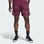 A person is wearing adidas Climacool Ergo Pro Men’s Badminton Shorts in maroon, featuring the adidas logo, paired with black adidas socks and black and white athletic sneakers. The ergonomic sports shorts utilize Climacool technology for enhanced breathability. The background is a solid light gray.