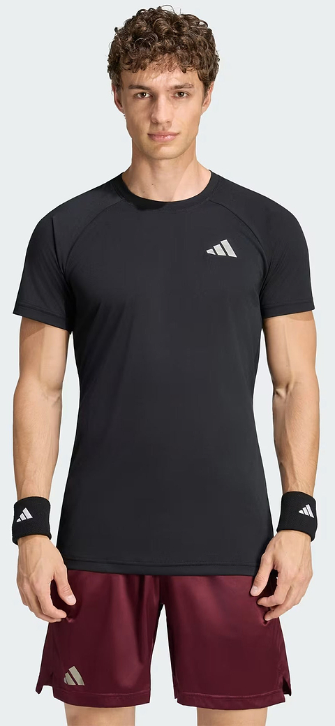 A man stands facing forward against a plain light background, wearing the adidas ADIDAS Climacool+ Freelift Pro Men’s Badminton T-Shirt in black, which features advanced cooling technology and a white adidas logo, paired with black wristbands and maroon shorts.