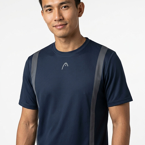 A man in a HEAD Club Tech 25 Men's Badminton T-Shirt in navy with gray stripes and a small chest logo stands against a white background, smiling slightly. This HEAD shirt features moisture-wicking fabric for breathable comfort.