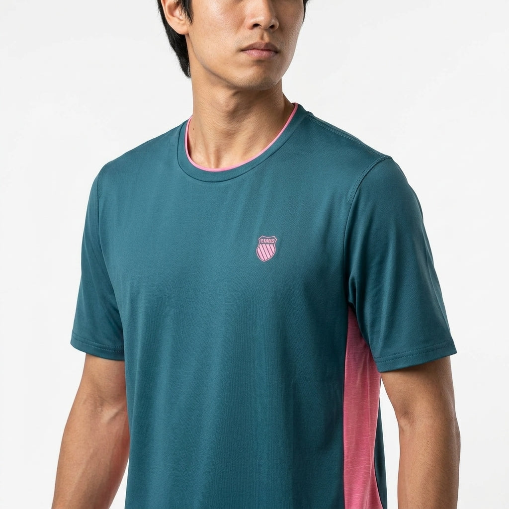 A man in the K-Swiss Hypercourt Mix Melange Men's Badminton T-Shirt in Stargazer/Pink, featuring pink side panels and a chest emblem, stands against a plain white background.