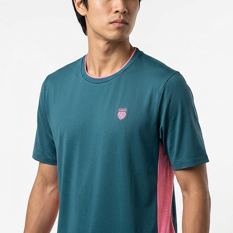 A man in the K-Swiss Hypercourt Mix Melange Men's Badminton T-Shirt in Stargazer/Pink, featuring pink side panels and a chest emblem, stands against a plain white background.