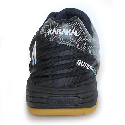 The image presents the rear view of the black Karakal Super Pro Indoor Court Badminton Shoes, highlighting an asymmetric lace system and hexagonal design, accompanied by "SUPER" text on the side. These indoor court shoes combine style and performance with a gum-colored sole and prominently feature the Karakal brand name on both the heel and sole.