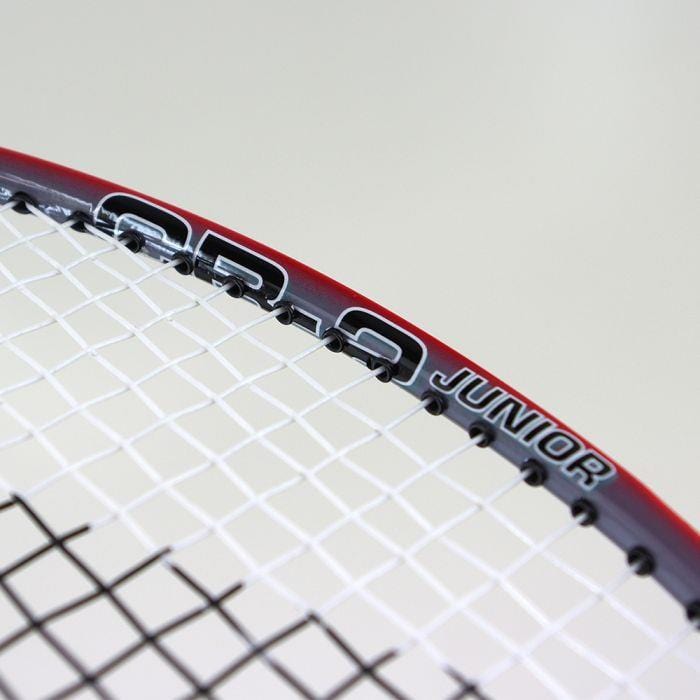 A close-up of the Karakal CB-2 Junior Badminton Racket showcases its aluminum head and striking black and red frame. The word "JUNIOR" is prominently displayed on the frame near the white strings, which are intricately arranged in a grid pattern. This sleek design is accentuated against a neutral background.