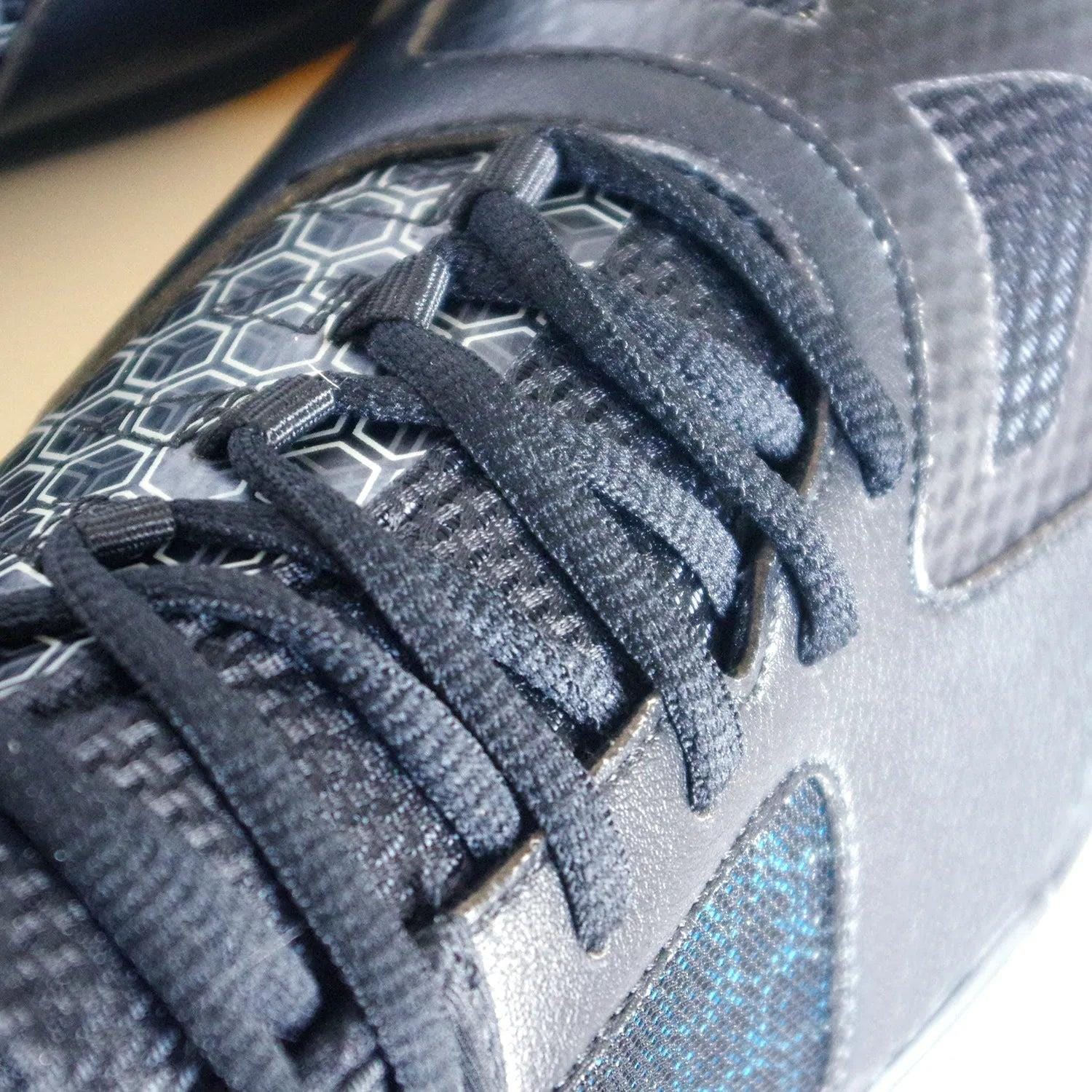 Close-up of the Karakal Super Pro Indoor Court Badminton Shoes in black, highlighting its textured fabric, asymmetric lace system, and hexagonal pattern detail near the eyelets, all contributing to a sleek and modern design.