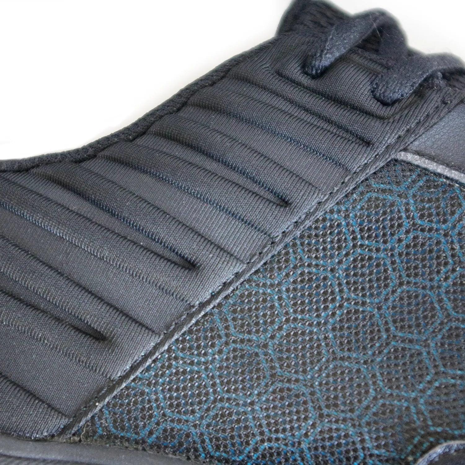 Close-up of the Karakal Super Pro Indoor Court Badminton Shoes in black, showcasing a textured black fabric with a hexagonal pattern and smooth, ribbed detailing on the upper part, enhanced by an asymmetric lace system.