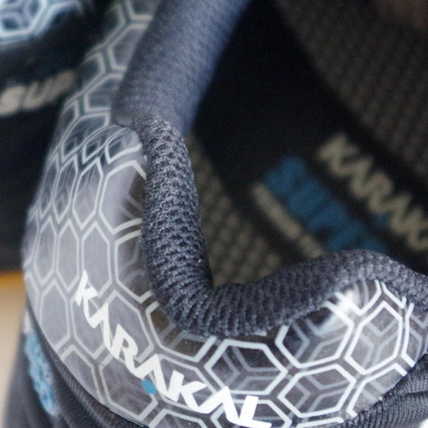 Close-up of a black Karakal Super Pro Indoor Court Badminton Shoe, showcasing its textured, hexagonal-patterned surface. The shoe prominently displays the "Karakal" branding on its side and features an asymmetric lace system. Constructed with a blend of fabric and synthetic overlays, it is designed for optimal performance during indoor court play.