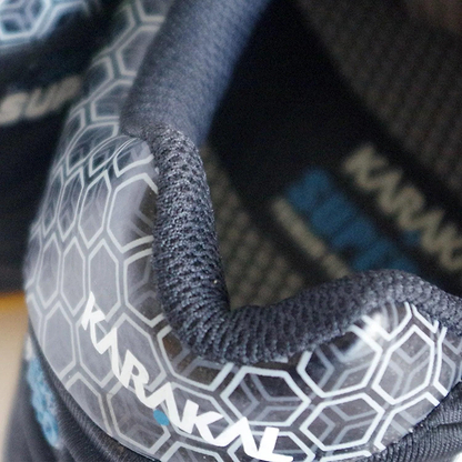 Close-up of a black Karakal Super Pro Indoor Court Badminton Shoe, showcasing its textured, hexagonal-patterned surface. The shoe prominently displays the "Karakal" branding on its side and features an asymmetric lace system. Constructed with a blend of fabric and synthetic overlays, it is designed for optimal performance during indoor court play.